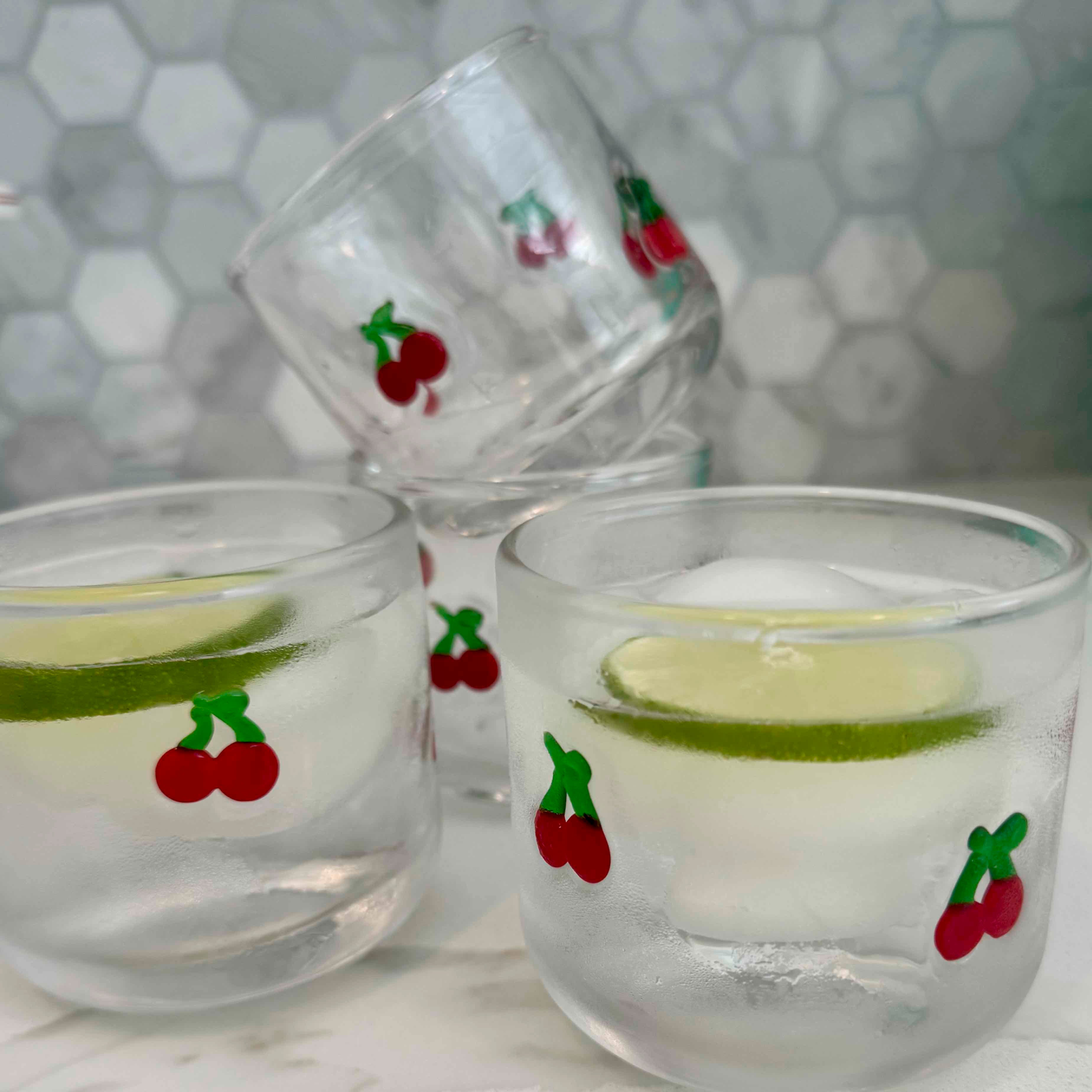 Clear glasses with cherry and lime decorations on a marble surface.
