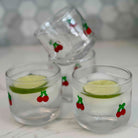 Three small glasses with lime slices and cherry decorations on a white surface.