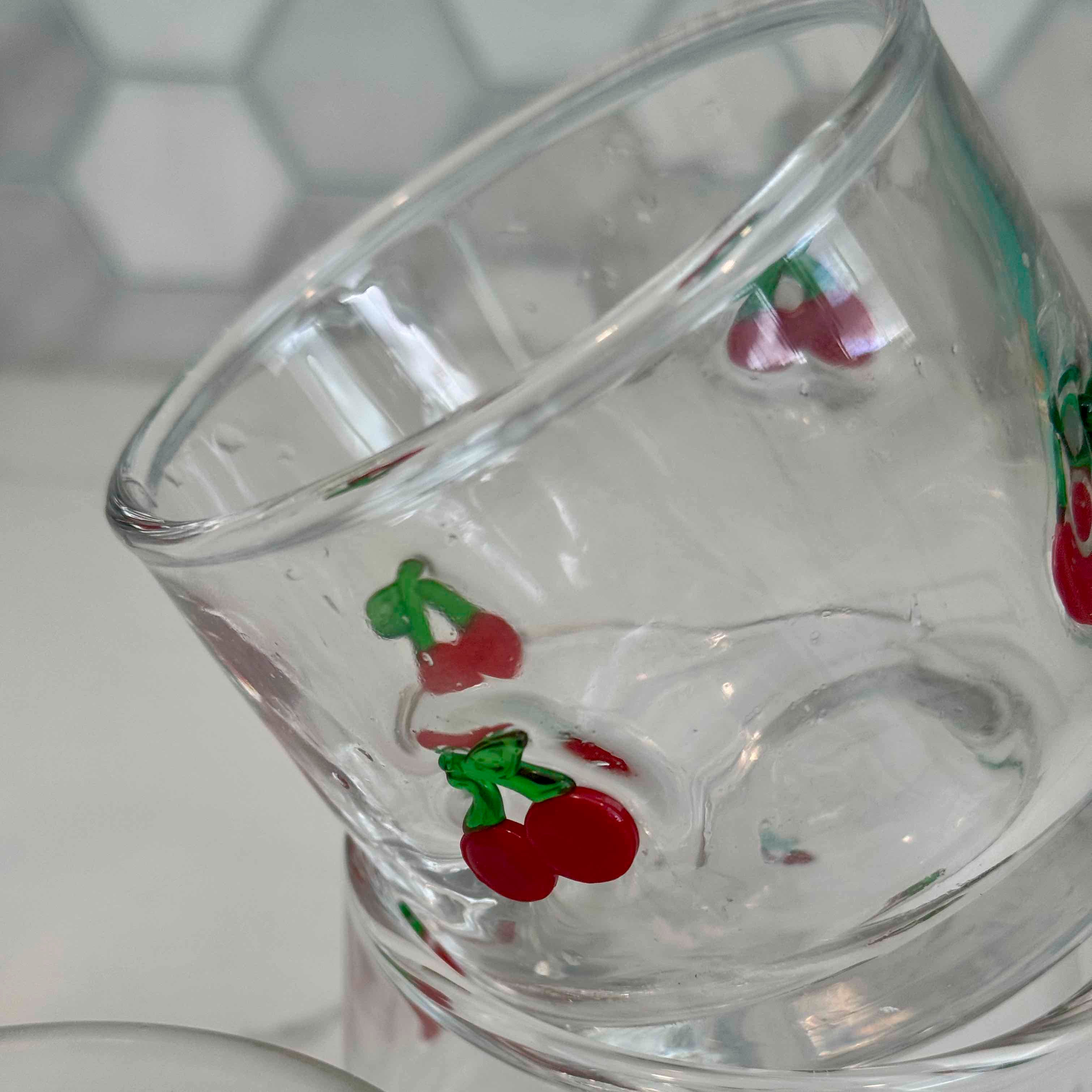 Clear glass tumbler with cherry designs on a white surface