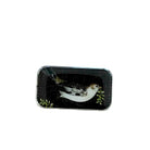 A rectangular tin with rounded corners, featuring a vintage-style bird illustration on a black background with green leaves, placed on a light wood surface.