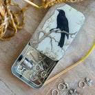 Tin box with a crow design on a wooden surface with jewelry items.