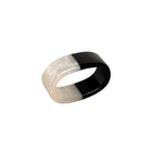 A wide band ring with a split design, featuring a textured translucent off-white outer half and a smooth glossy black inner half, resting on a gray textured surface.