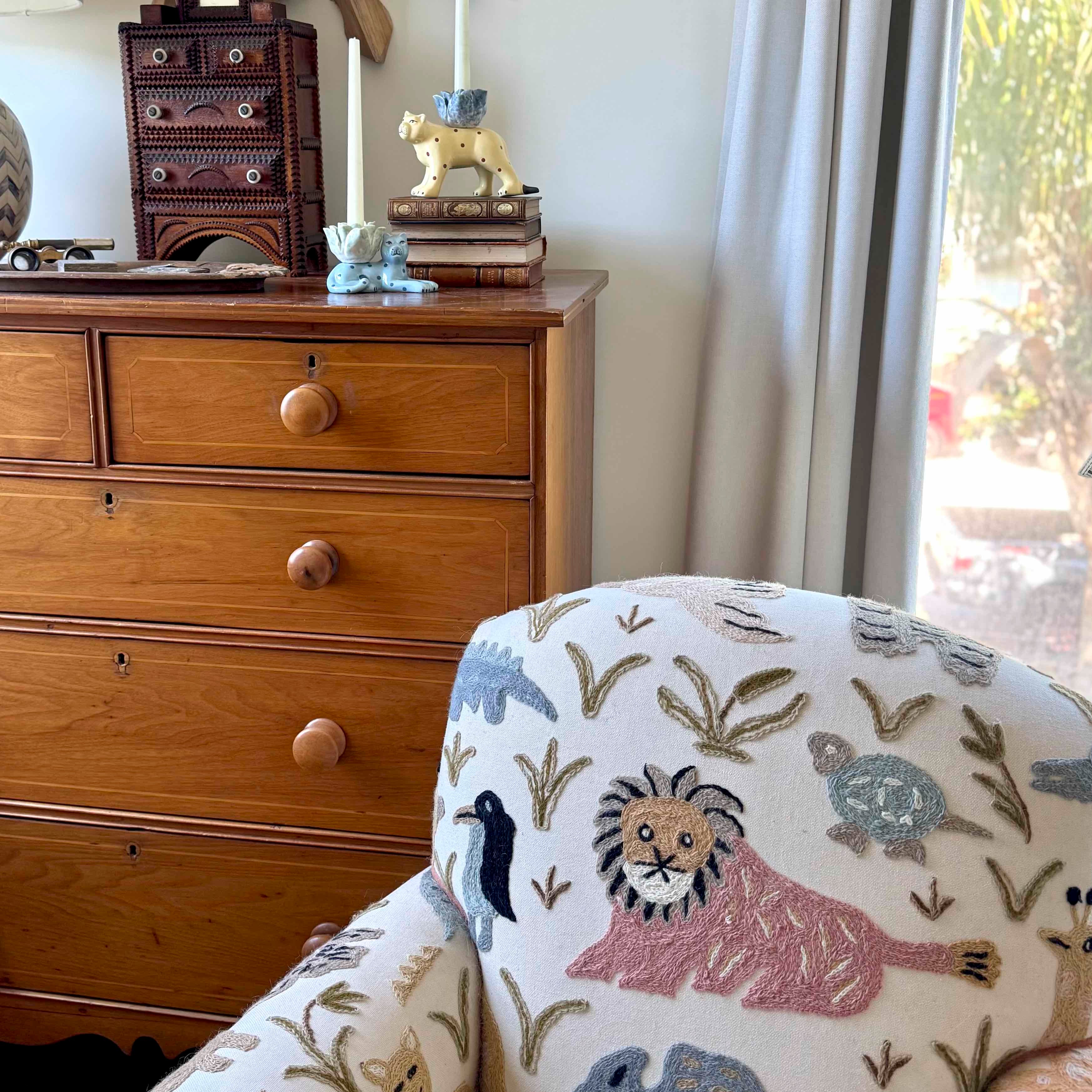 Chair with embroidered design in a room with wooden dresser and window.