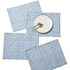 Set of four blue floral placemats with a white plate and gold fork on a white background
