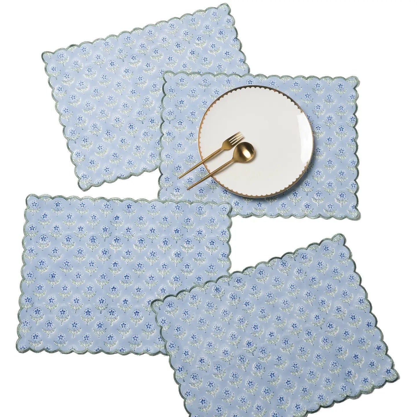Set of four blue floral placemats with a white plate and gold fork on a white background