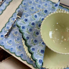 Set of green ceramic plates and bowls on a floral-patterned blue placemat.
