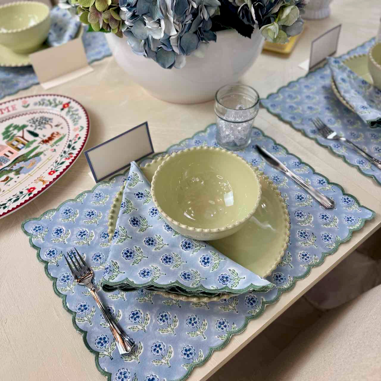 Dining table setting with floral placemats, green bowls, and cutlery.