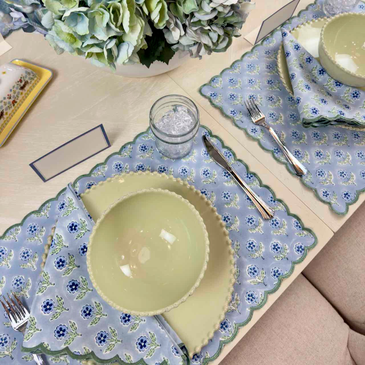 Dining table setting with floral placemats, green bowls, and cutlery.
