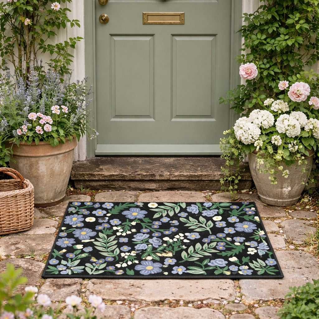 Floral doormat in front of a green door with potted plants on either side.
