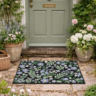Floral doormat in front of a green door with potted plants on either side.