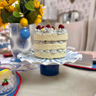Layered cake with berries on a blue and white cake stand in a dining setting.