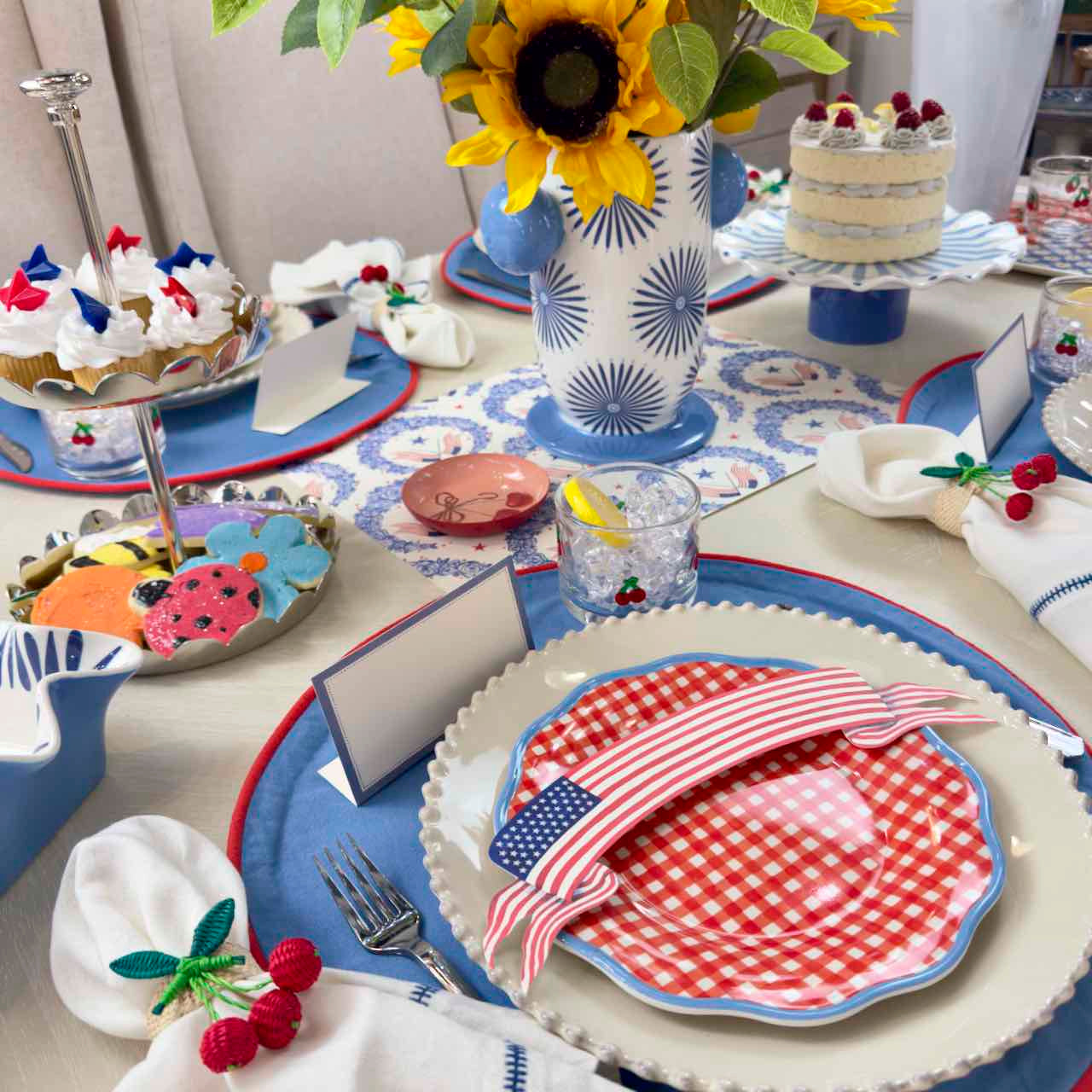 Dessert table with colorful plates, sunflower centerpiece, and patriotic decorations.