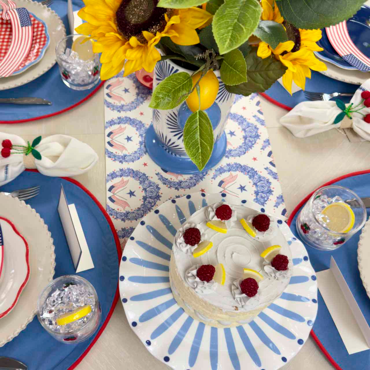 Decorative table setting with sunflowers, lemon slices, and a small cake on a blue and white plate.