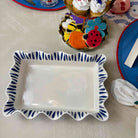 Rectangular ceramic dish with blue decorative border on a table with colorful items in the background