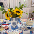 Decorative table setting with sunflowers in a patterned vase, cake, and colorful plates.