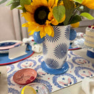 Decorative table setting with sunflowers in a patterned vase on a festive tablecloth.