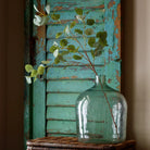 Clear glass vase with greenery against a rustic wooden background