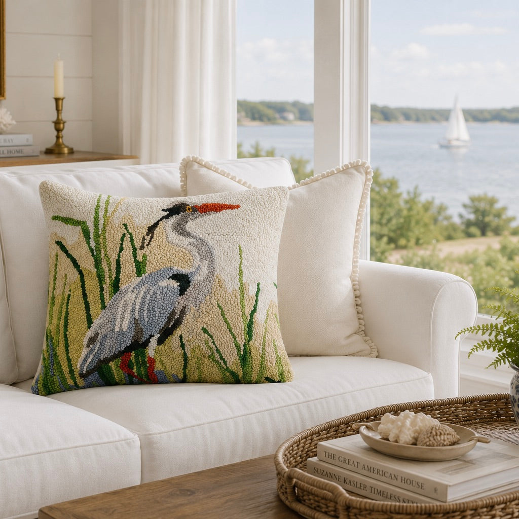Decorative pillow with a heron design on a white couch in a room with large windows overlooking water.