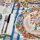 Table setting with floral tablecloth, plates, cutlery, and napkin on a checkered tablecloth.