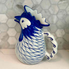 Blue and white ceramic rooster mug on a light gray surface with a geometric patterned wall in the background.
