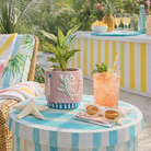 Outdoor setting with a striped table, plant, drink, sunglasses, and pineapple.