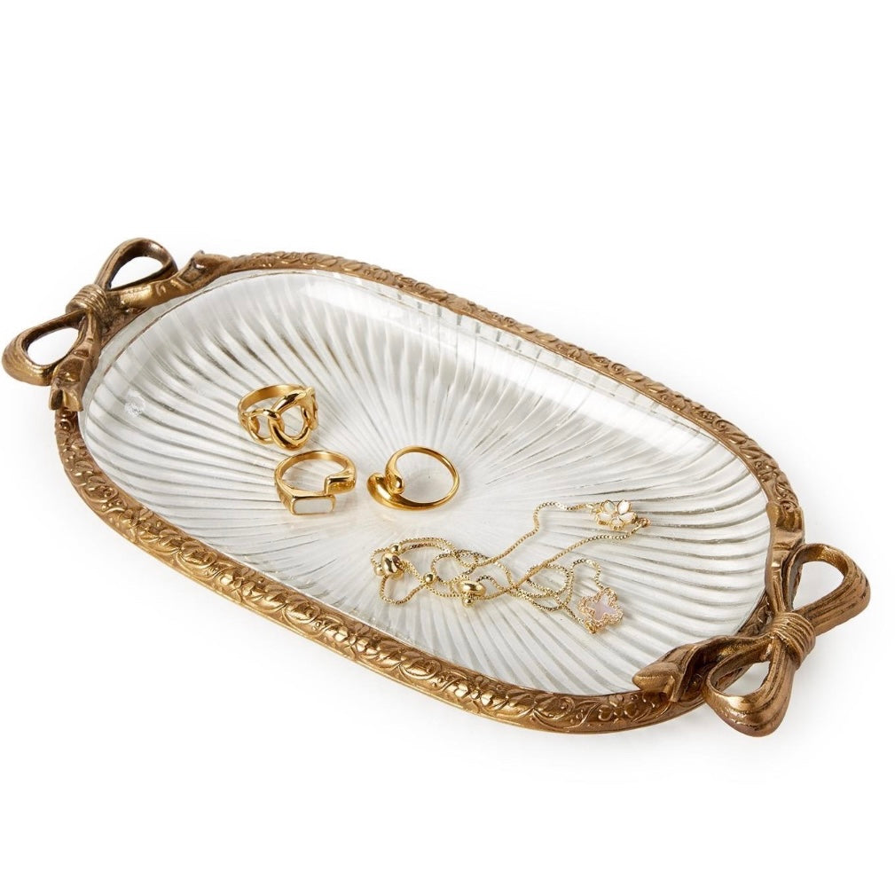 An oval decorative jewelry tray with a ribbed white center and an ornate gold-toned border, shown holding several gold rings and a necklace on a clean white background.