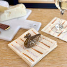 Decorative gold duck on a napkin with a glass of white wine and cheese plate in the background.
