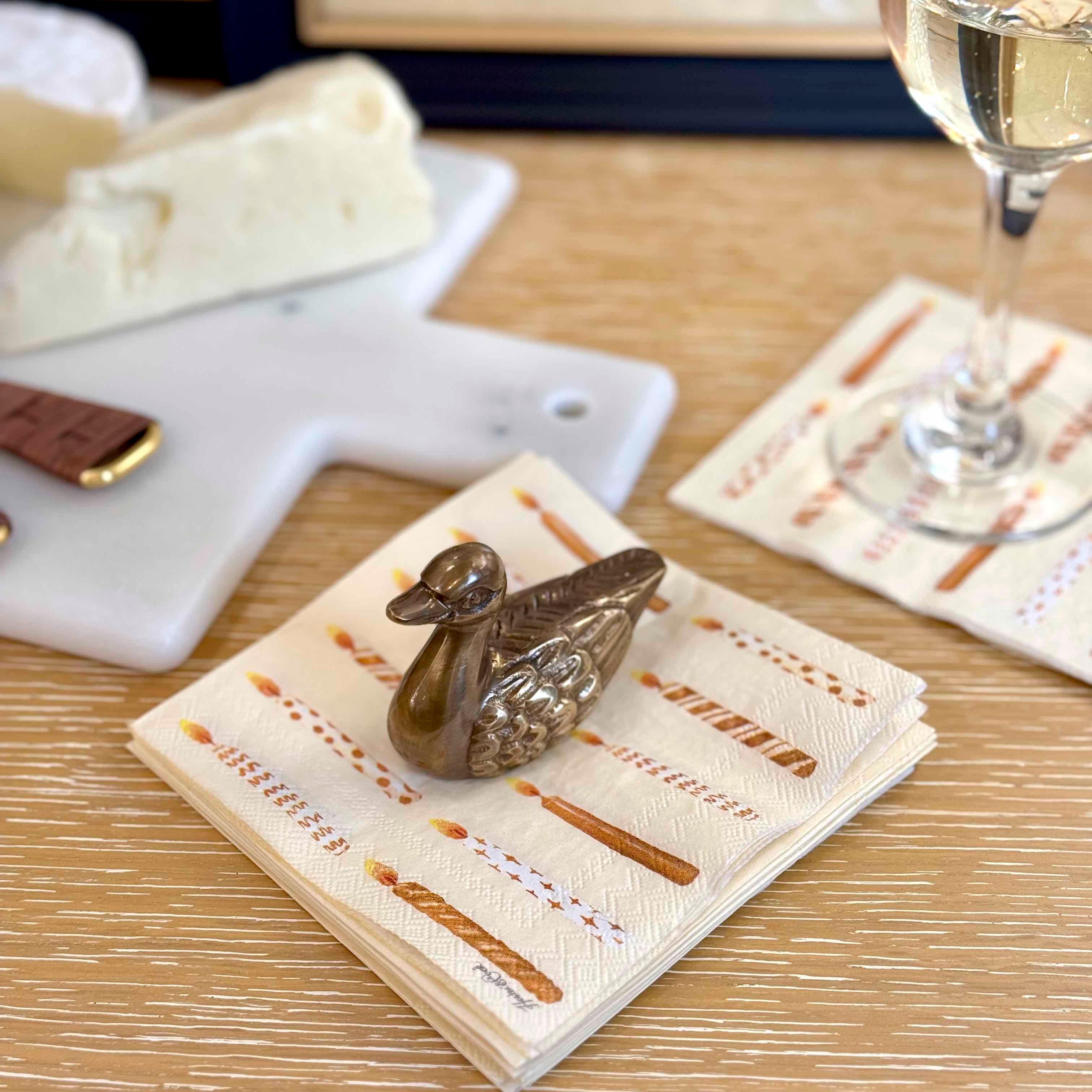 Decorative gold duck on a napkin with a glass of white wine and cheese plate in the background.