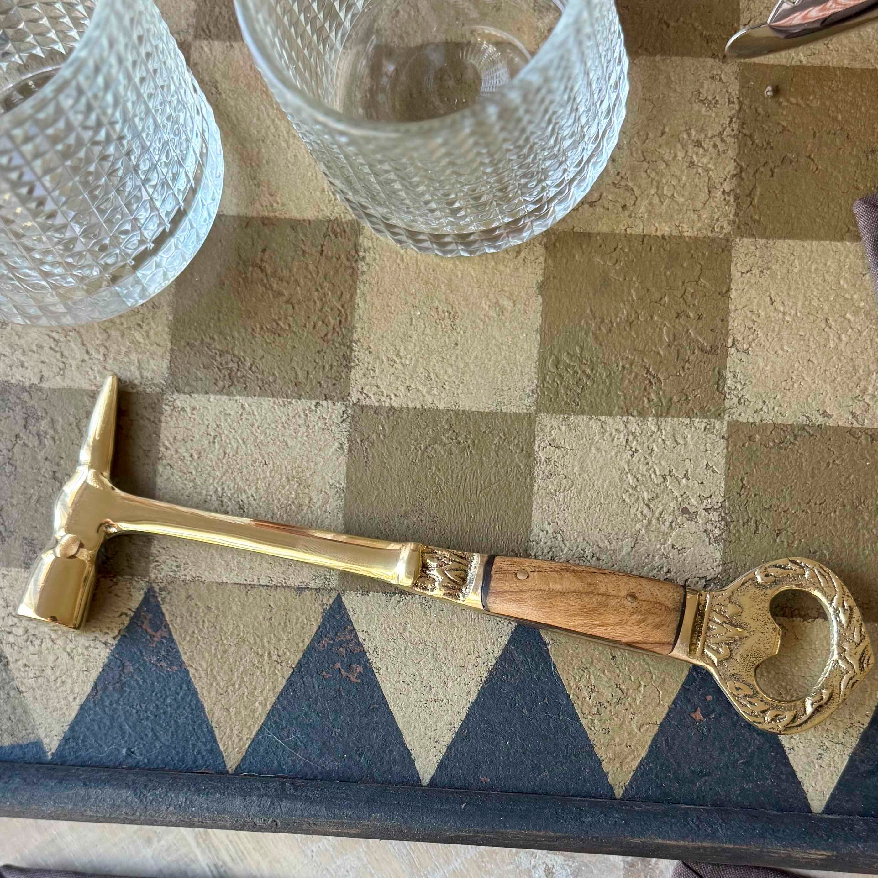 Decorative key-shaped tool on a checkered surface with glasses in the background