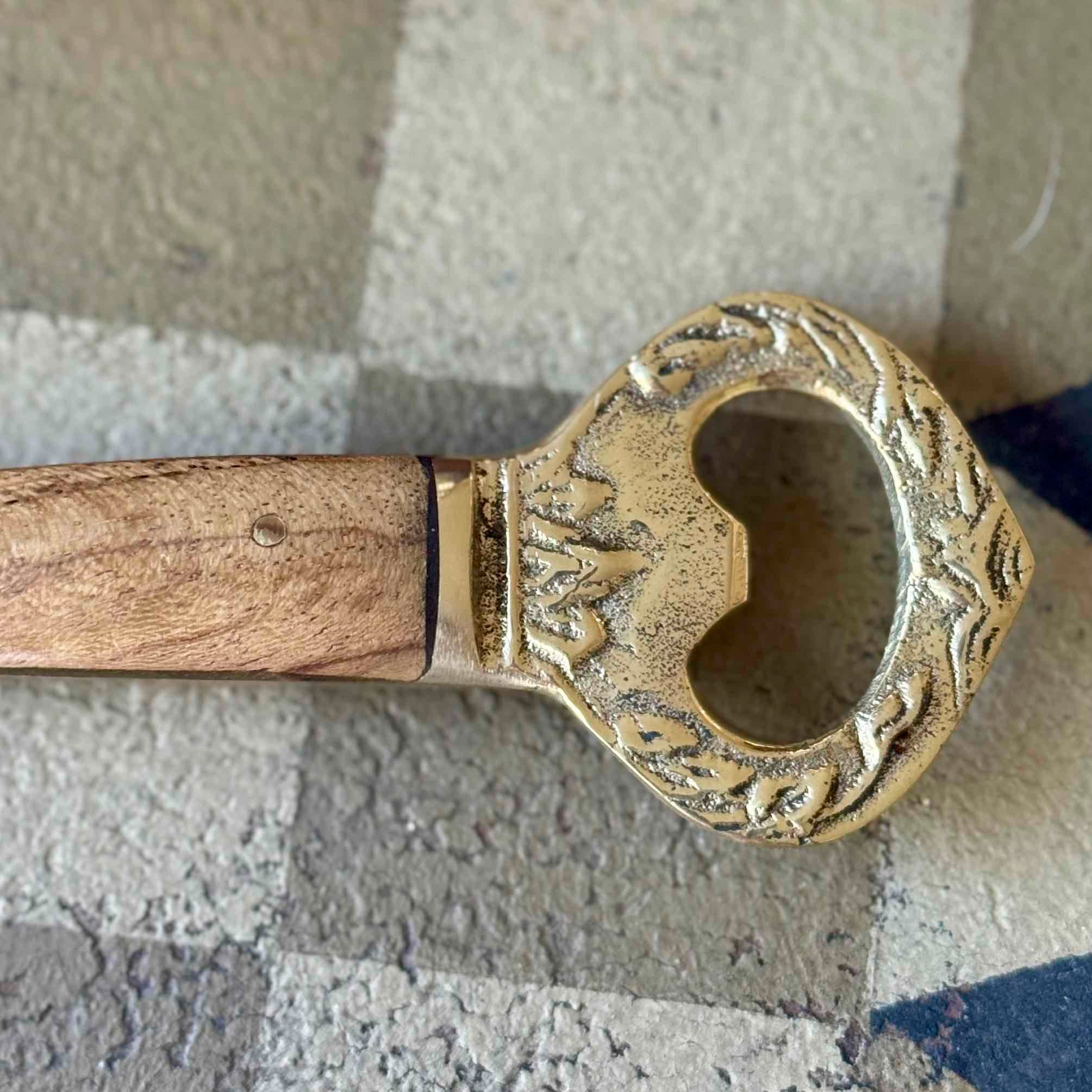 Decorative bottle opener with wooden handle and ornate metal design on a textured surface.