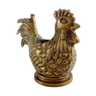A decorative rooster figurine in a distressed antique brass or bronze finish, featuring a textured body, detailed feathers, and a circular base, set against a plain white background.