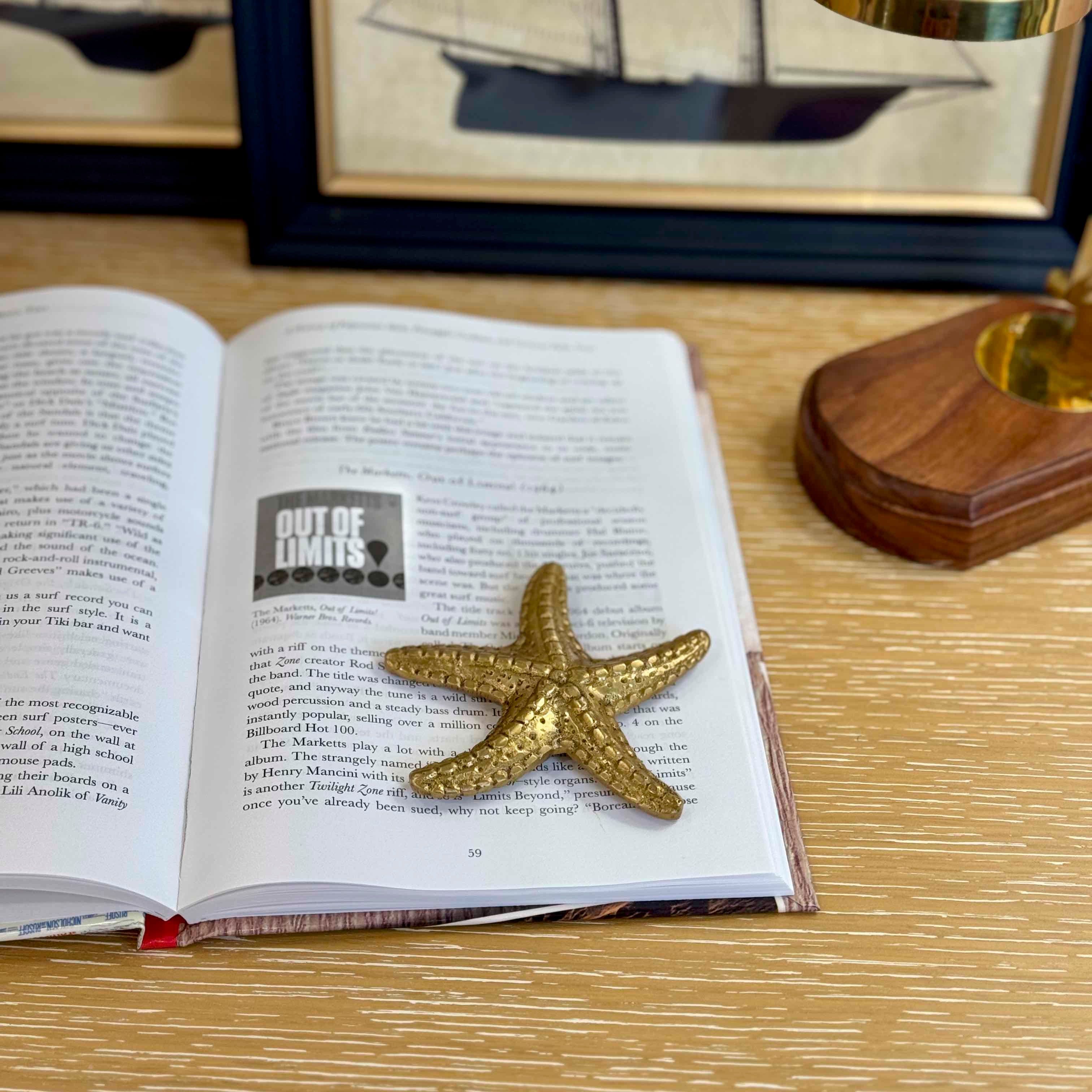 Gold starfish on an open book with a framed picture and decorative object in the background.