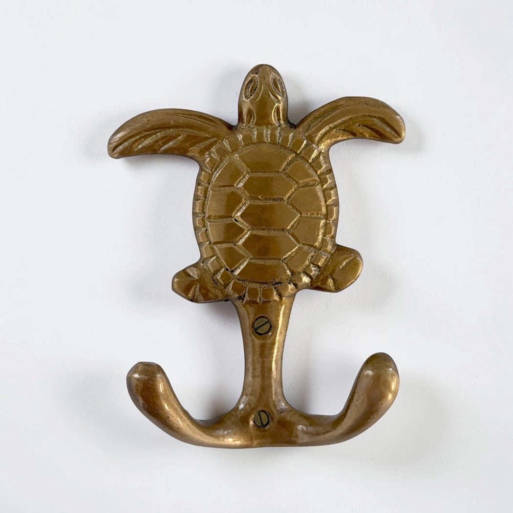 A brass turtle-shaped wall hook with a textured shell and flared wings, mounted on a plain white background.