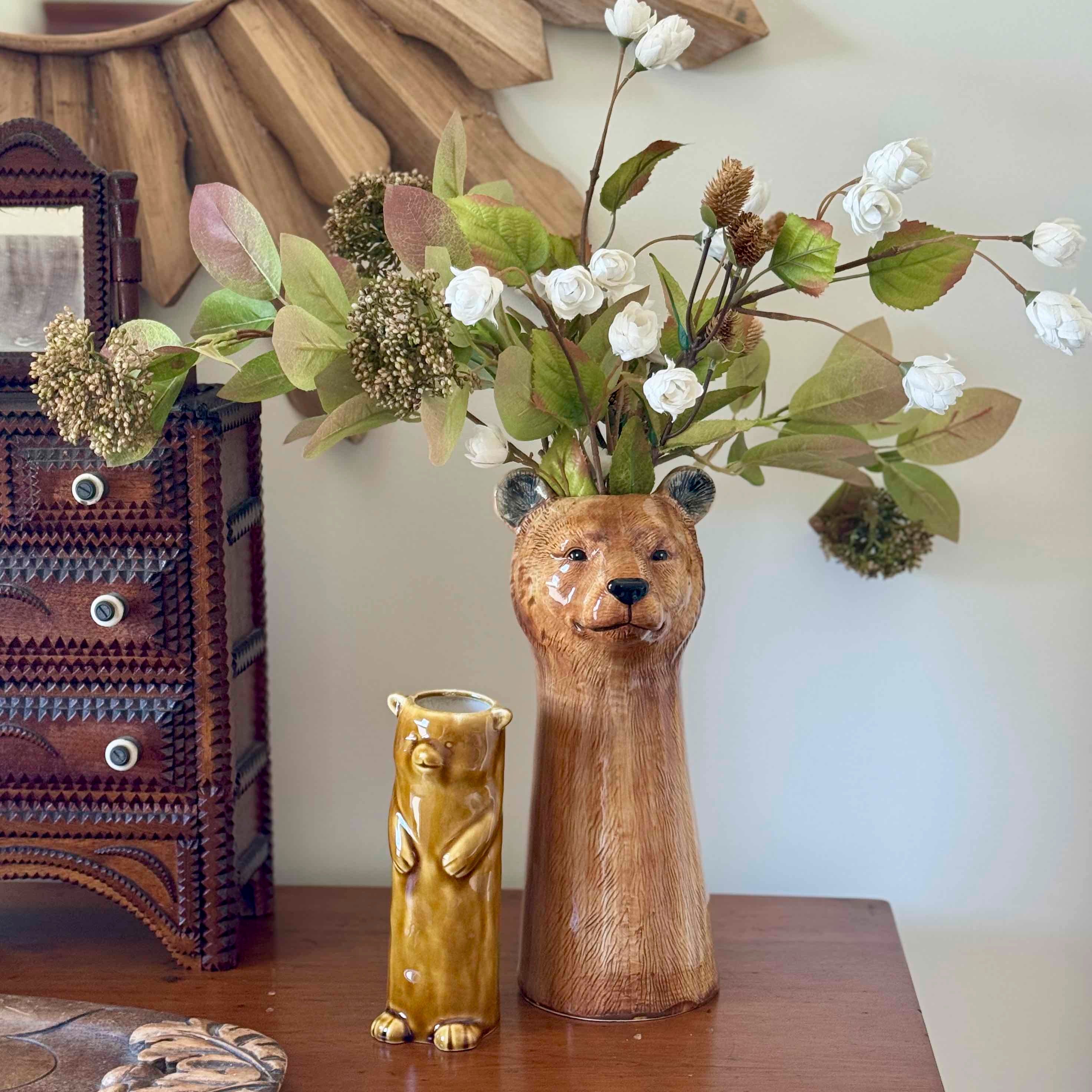 Wooden bear-shaped vase with flowers on a wooden surface next to a decorative dresser.