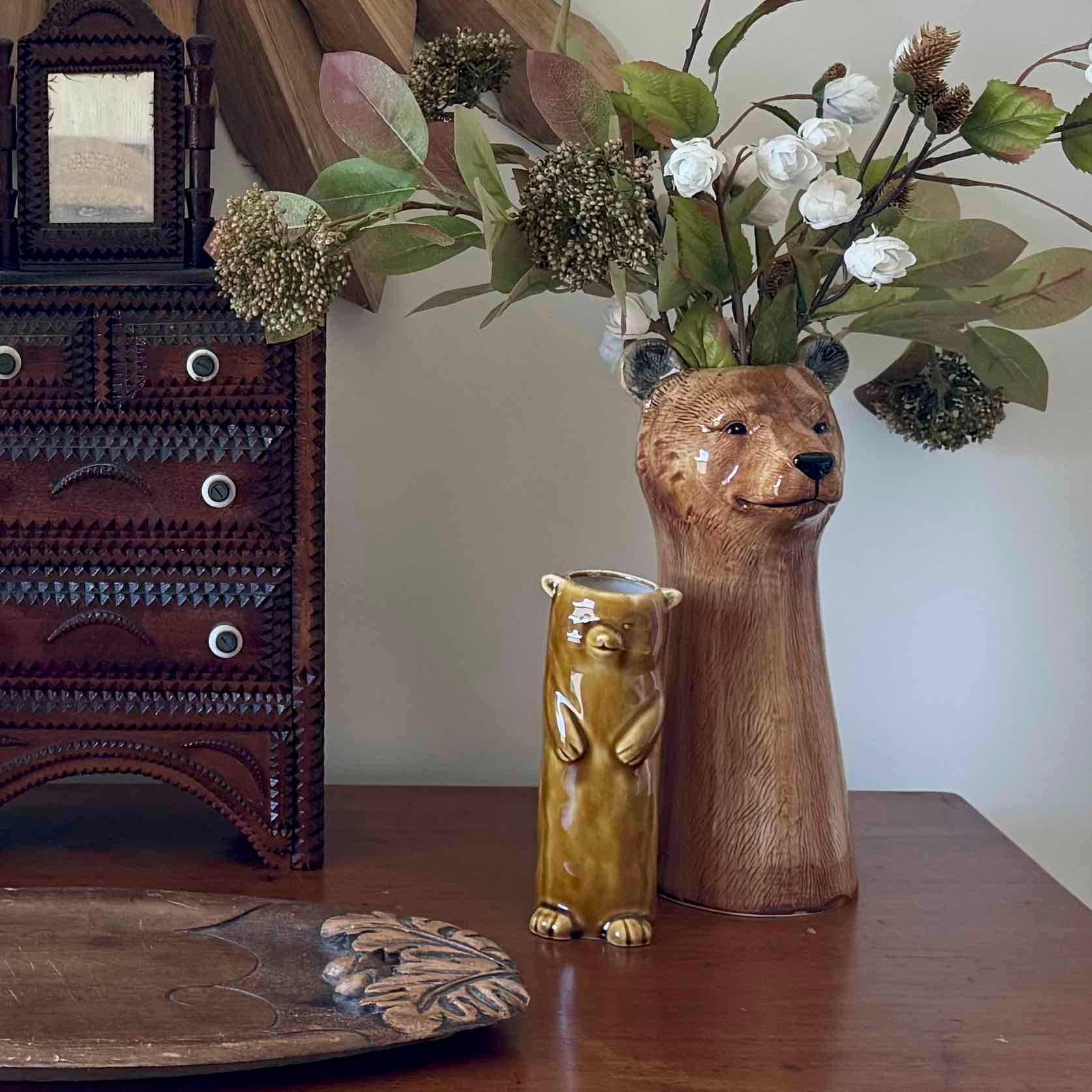 Bear-shaped vase with flowers on a wooden surface next to a decorative cabinet.