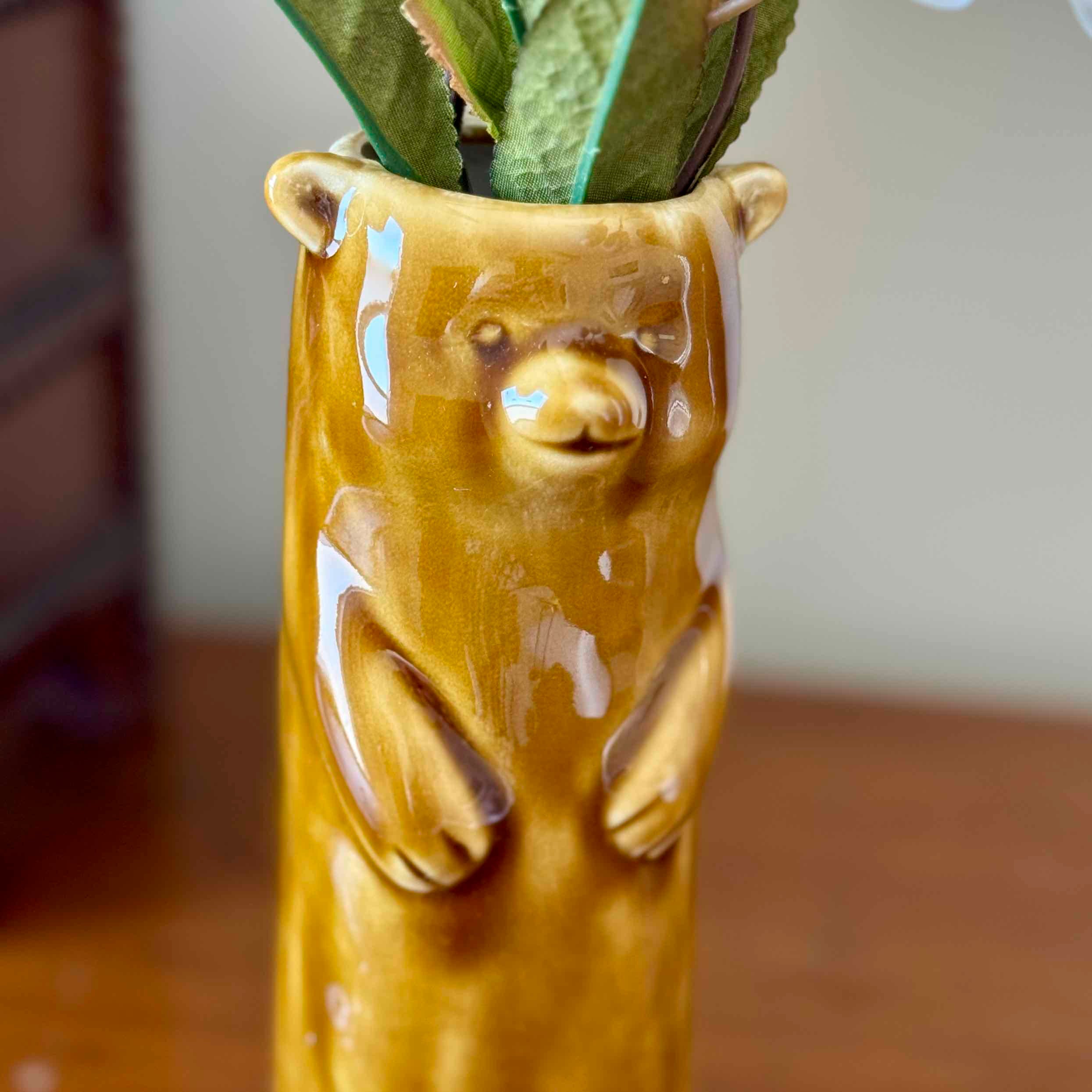 Yellow bear-shaped vase with a plant inside on a wooden surface.