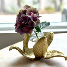 Decorative gold leaf holder with a vase of purple flowers on a light surface.