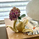 Decorative gold vase with a pink flower on a wooden surface