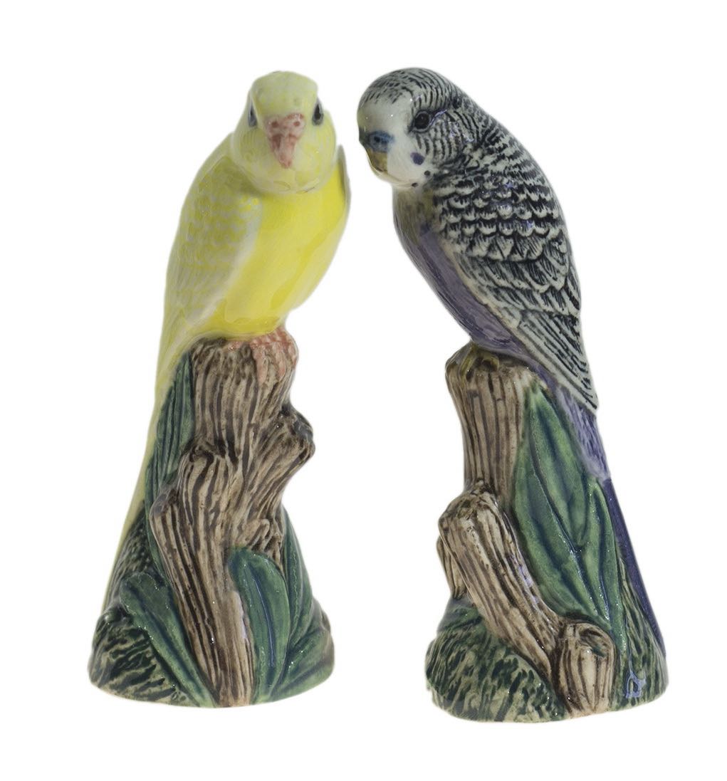 Two ceramic parakeets on a branch with a white background