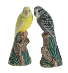 Two ceramic parakeets on a branch with a white background