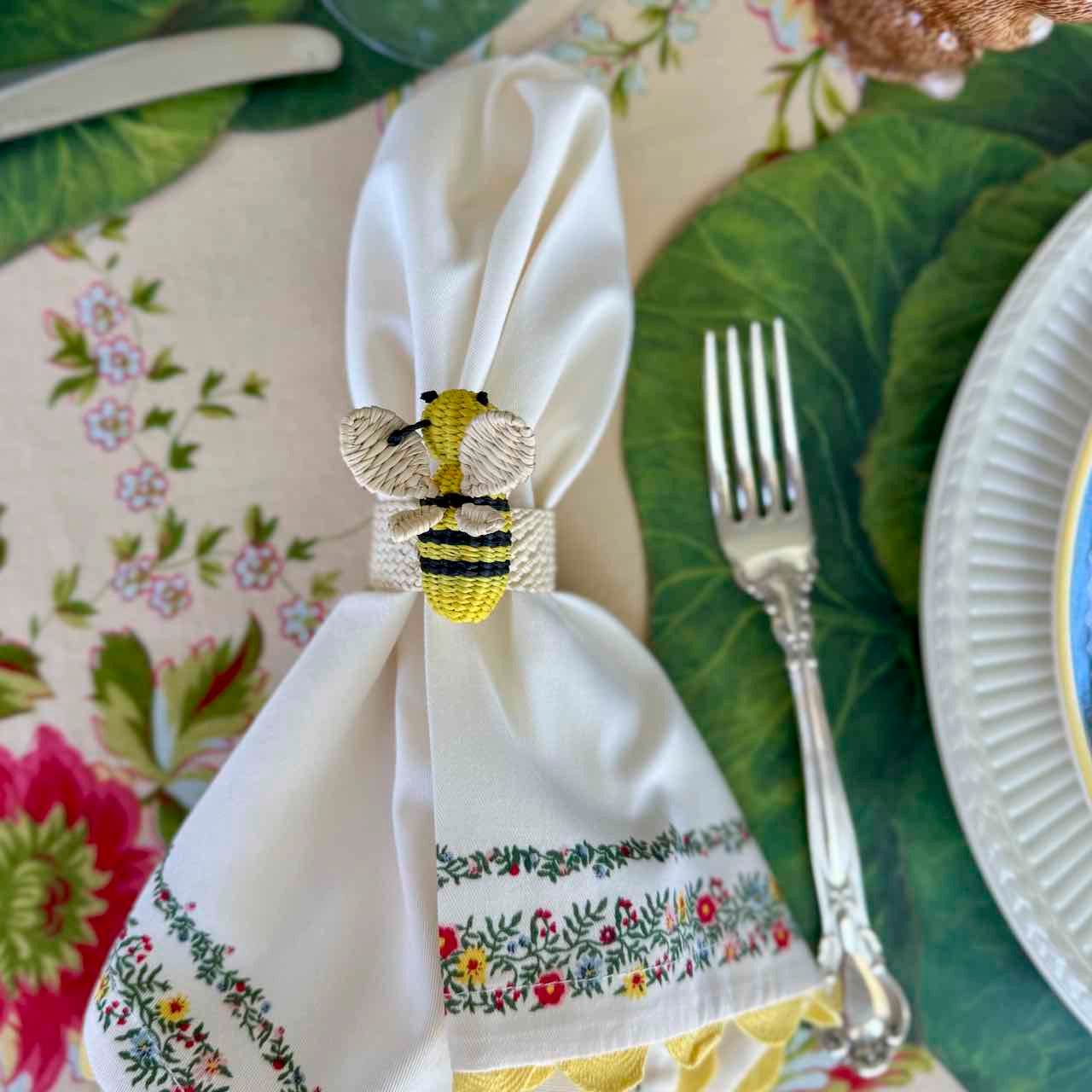 Napkin with embroidered designs and a bee-themed napkin ring on a table setting.