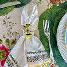 Napkin with embroidered designs and a bee-themed napkin ring on a table setting.