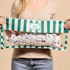 Woman holding a green and white striped bag with small boxes inside on a beige background