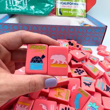 Hand holding a pink game piece with 'Joker' on it, surrounded by more pink game pieces.