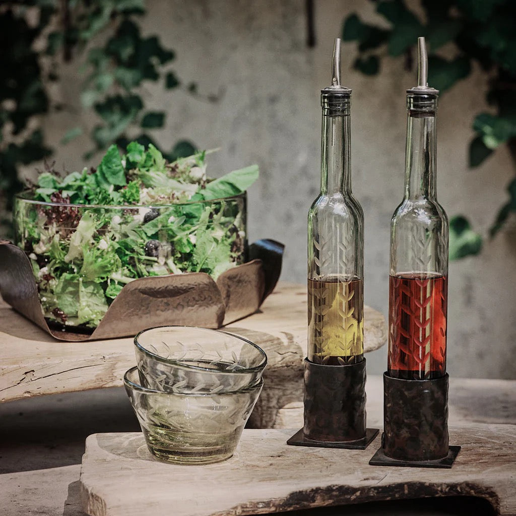 Two glass oil and vinegar bottles on a wooden surface with a salad in the background.