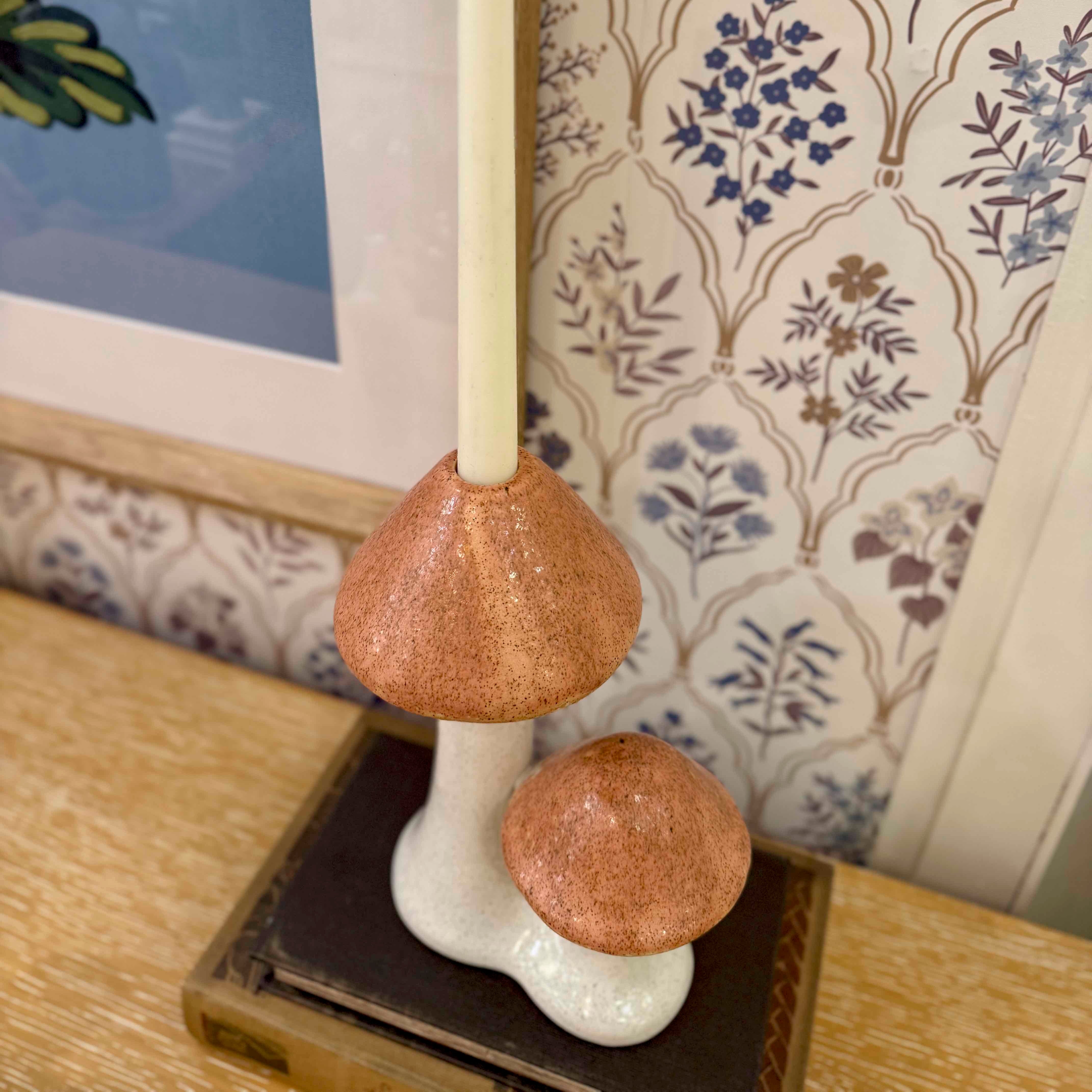 Mushroom-shaped candle holder on a wooden surface with floral wallpaper in the background