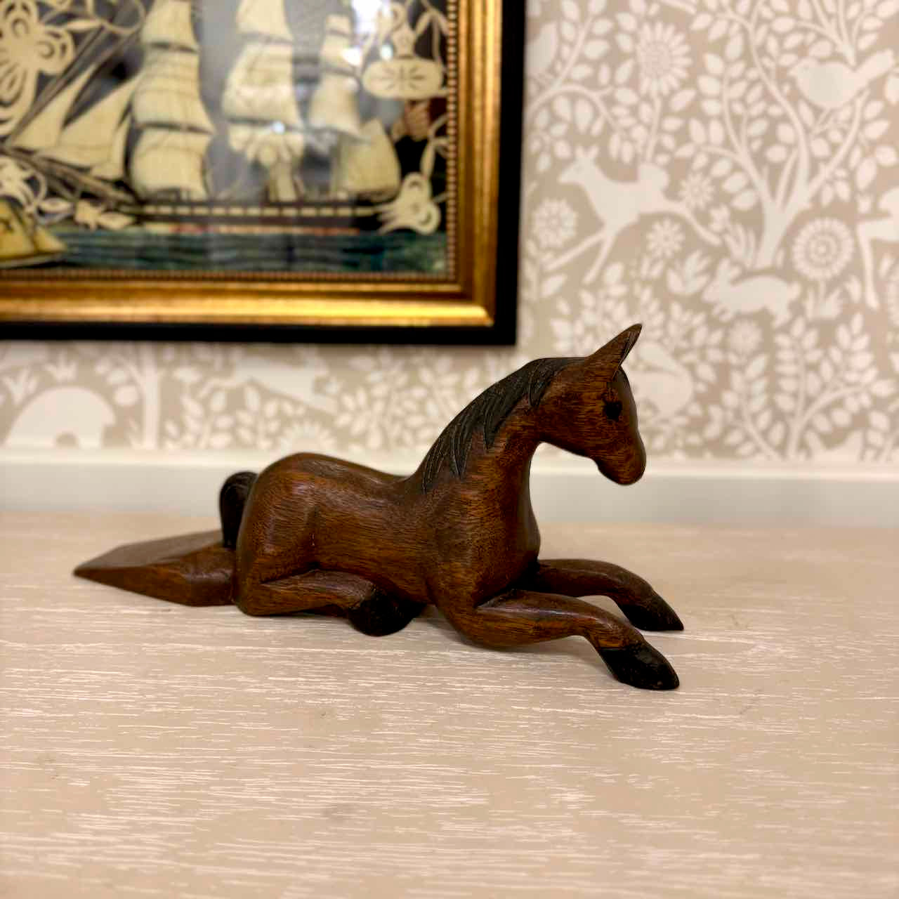 Wooden horse figurine on a wooden floor with a decorative wall in the background