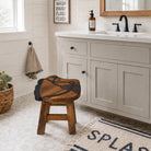 A rustic wooden bathroom stool with a carved animal face design sits in front of a white vanity in a bright, modern bathroom.