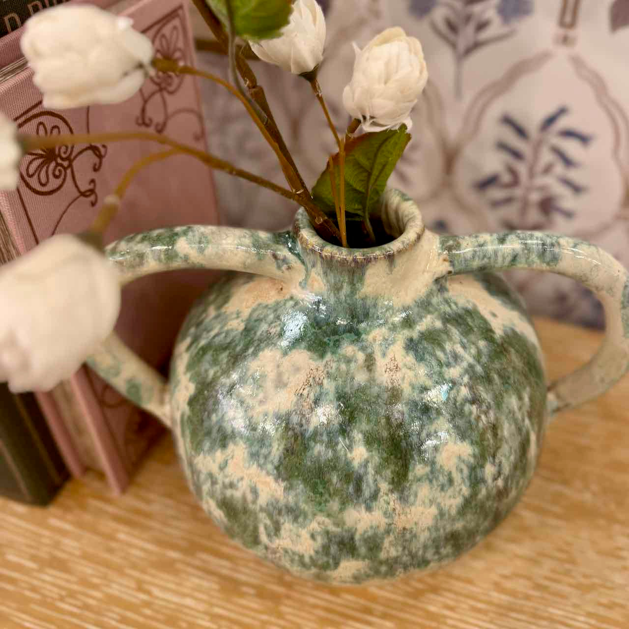 Green ceramic vase with floral arrangement on a wooden surface