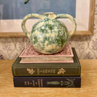 Green ceramic vase on top of two books with a decorative background
